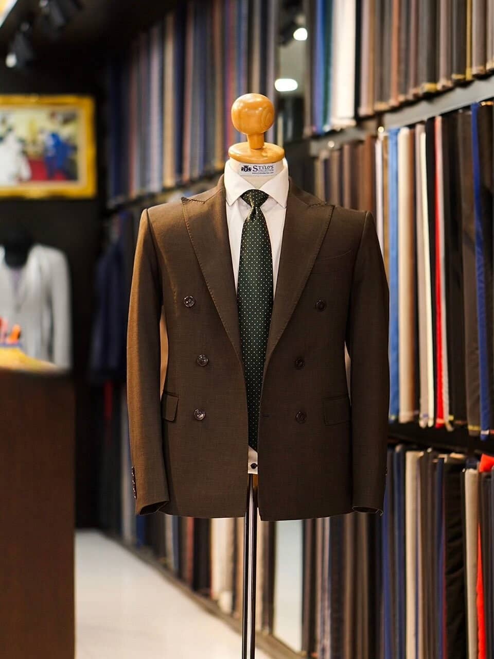Brown double-breasted suit on a mannequin in front of the fabric wall at the Stylo's Collection showroom